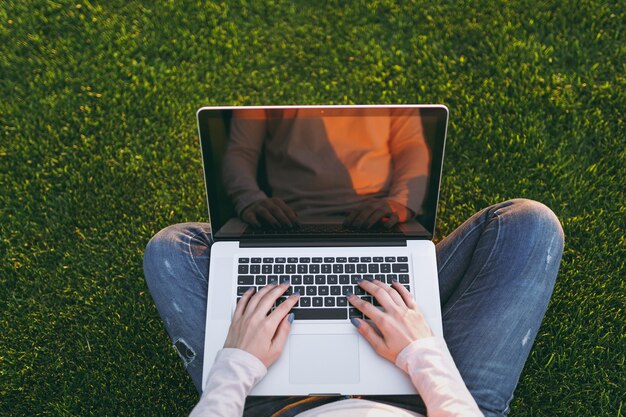 Vue de dessus au-dessus des mains sur le clavier. Femme travaillant sur un ordinateur portable avec un écran vide noir vierge pour copier l'espace sur la pelouse d'herbe verte ensoleillée à l'extérieur. Bureau mobile. Concept d'entreprise indépendant.