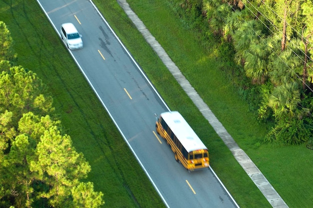Vue de dessus de l'autobus scolaire jaune américain classique conduisant dans la rue de la ville rurale pour aller chercher les enfants pour leurs leçons tôt le matin Transports publics aux États-Unis