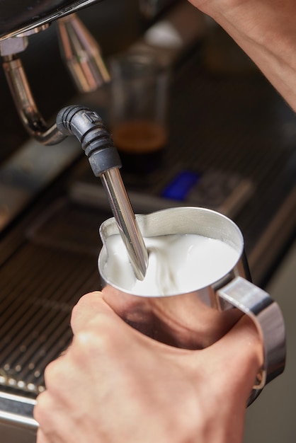 Vue de dessus d'un barista professionnel versant du lait du pot dans une tasse de café en cours de préparation