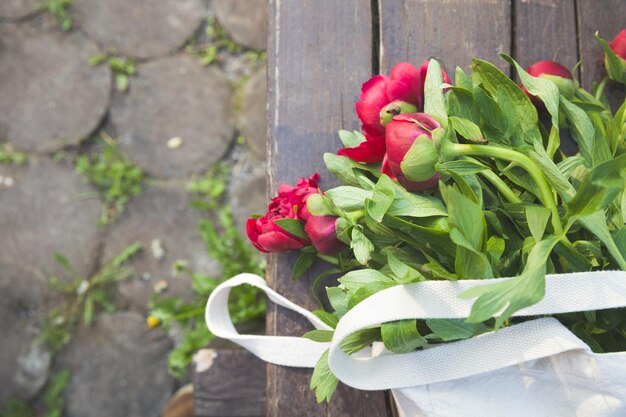 Vue de dessus sur un beau bouquet de pivoines rouges dans un sac textile sur le fond en bois