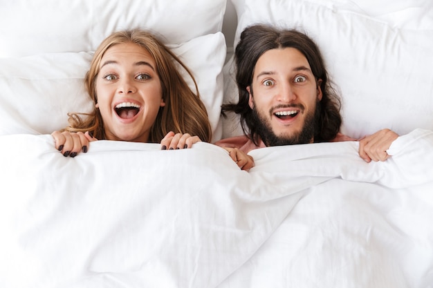 Vue de dessus d'un beau jeune couple excité conique dans une couverture allongée dans son lit à la maison