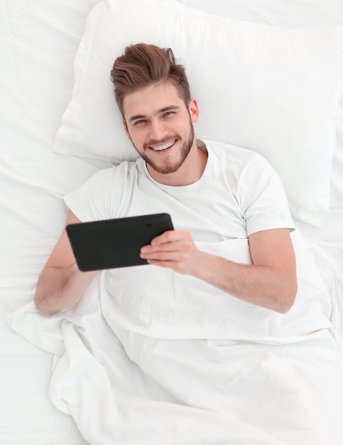 Vue de dessus bel homme tapant sur une tablette numérique allongé sur le lit