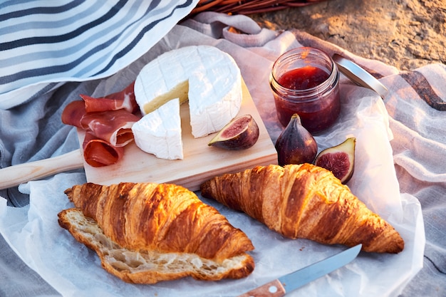 Vue de dessus de la belle composition de pique-nique romantique avec croissants, pain, confiture, fromage, figues et jamon.