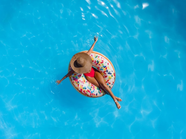 Vue de dessus d'une belle jeune femme dans la piscine nage sur un beignet gonflable et s'amuse en vacances.
