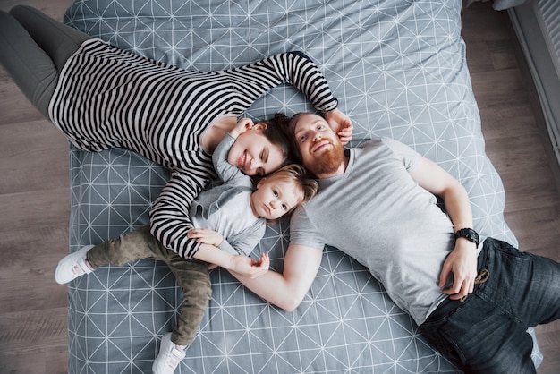 Vue de dessus de la belle jeune mère, père et leur fille regardant et souriant en position couchée sur le lit tête à tête