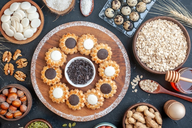 vue de dessus biscuits au chocolat et chocolat noir sur planche de bois bols avec noix avoine bonbons oeufs de caille en viol miel pot oeuf en coquetier sur table