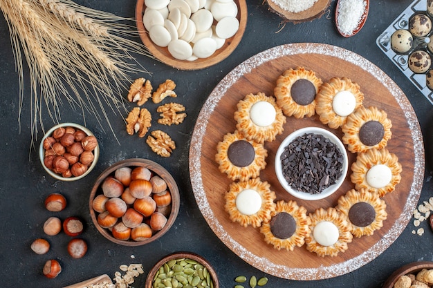 vue de dessus biscuits au chocolat et chocolat noir sur planche de bois bols avec noix bonbons oeufs de caille en viole sur table