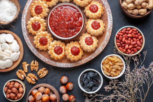 vue de dessus biscuits avec confiture et bol de confiture sur planche de bois noix de chocolat blanc dans des bols sur fond sombre