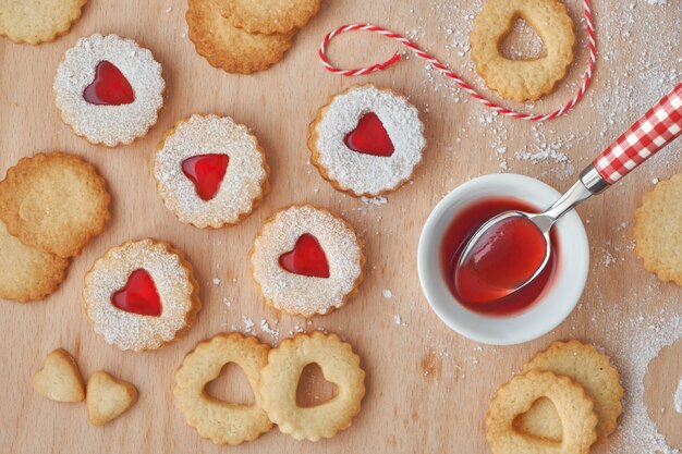 Vue de dessus des biscuits Linzer de Noël traditionnels remplis de confiture de fraises sur planche de bois.