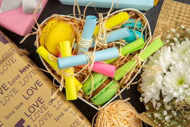 vue de dessus boîte en forme de coeur avec des notes autocollantes enroulées et des cadeaux enveloppés de macarons bouquet de fleurs sur la table