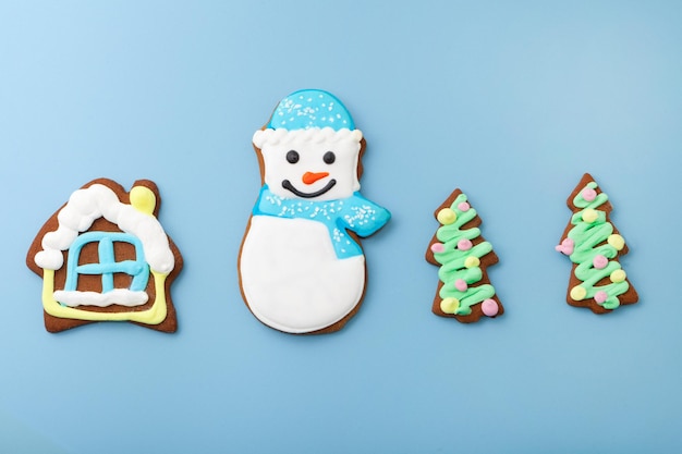 Vue de dessus de bonhomme de neige en pain d'épice et maison avec arbre de noël différents biscuits sur fond bleu