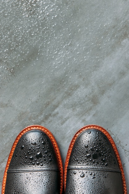 Vue de dessus des bottes pour hommes en cuir noir avec des gouttes d'eau sur fond bleu marine grunge