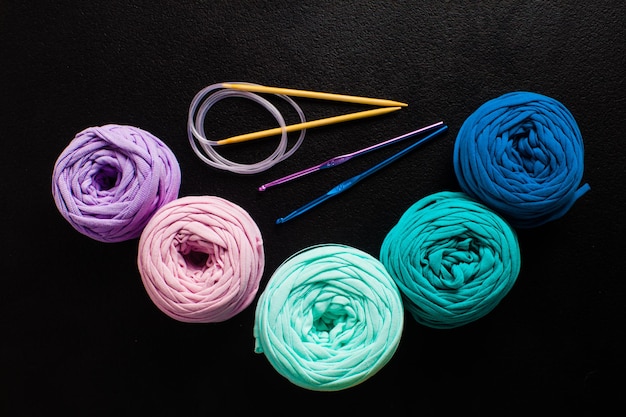 Vue de dessus des boules de fils textiles avec des aiguilles à tricoter et des crochets sur le noir. Passe-temps Nature morte, composition à plat, art passe-temps
