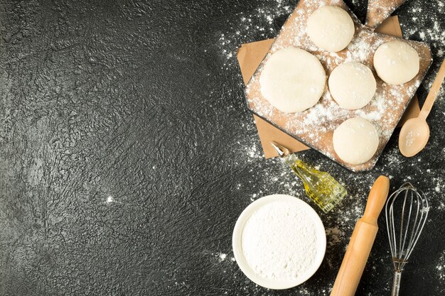 Vue de dessus des boules de pâte sur une plaque en bois avec des ingrédients de cuisson sur la table noire