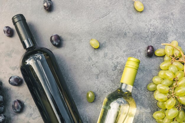 Vue de dessus de la bouteille de vin rouge et blanc, verre à vin de vigne verte et raisin mûr sur une table en pierre sombre vintage...