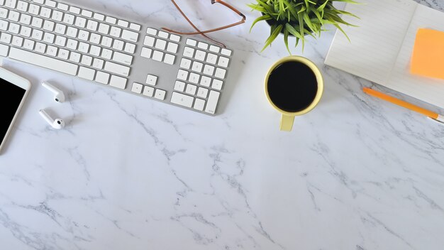 Vue de dessus bureau en marbre avec ordinateur, café, fournitures de bureau et téléphone portable.