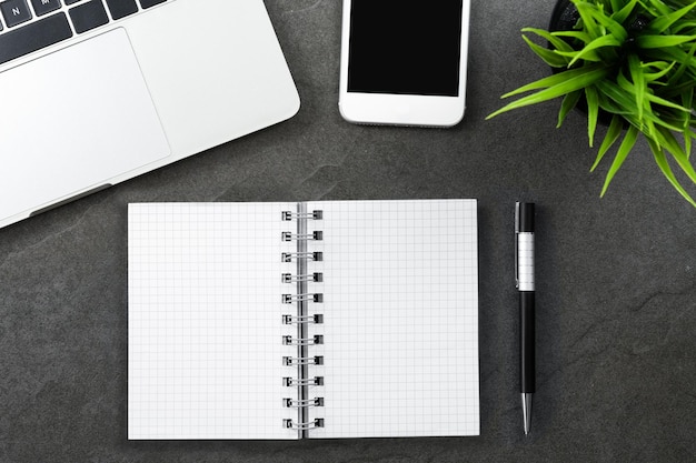 Vue de dessus d'un bureau sombre ou d'un bureau à domicile avec une plante verte pour smartphone et un cahier vierge