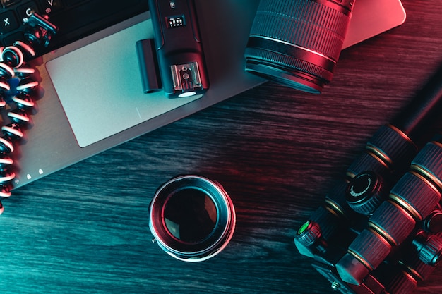 Vue de dessus d'un bureau travaillant avec un clavier d'ordinateur portable, un appareil photo moderne, un objectif, un trépied et un stylo