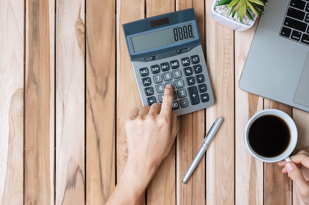 Vue de dessus Business woman hand holding coffee cup et calcul avec calculatrice, stylo et ordinateur portable sur table de bureau en bois