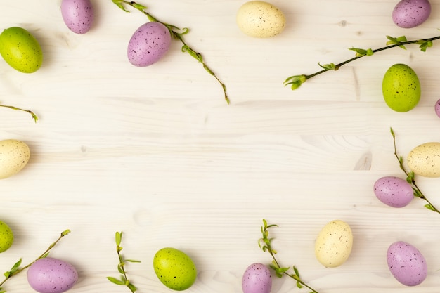 Vue de dessus d'un cadre d'oeufs de Pâques colorés et saule de printemps sur un fond en bois clair avec espace de message