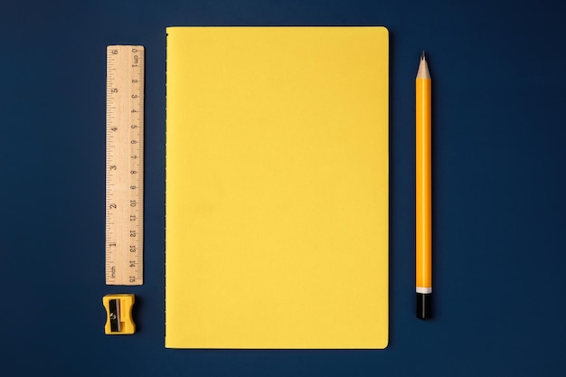 Vue de dessus cahier jaune pastel avec crayon jaune et bloc-notes sur une table de travail bleu marine