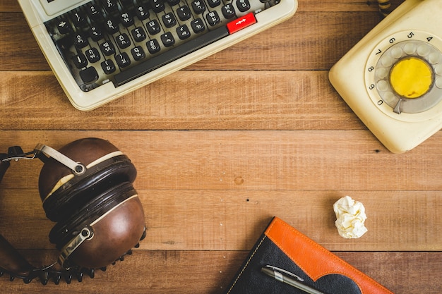 Vue de dessus de cahier sur la table en bois, machine à écrire, vieux téléphone et écouteur