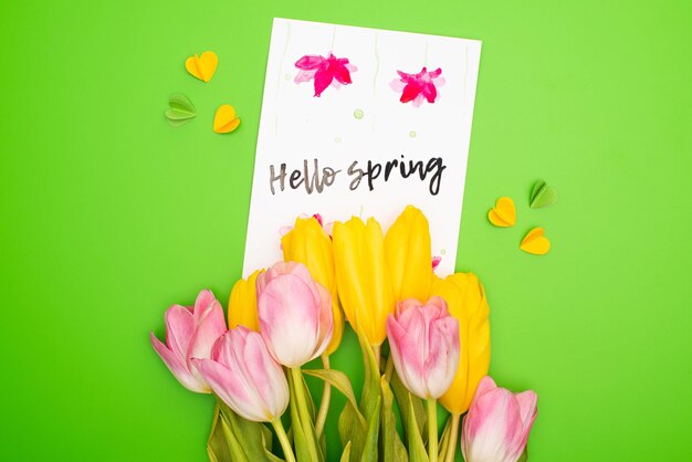 Vue de dessus de la carte bouquet avec lettrage de printemps bonjour et coeurs décoratifs sur rose