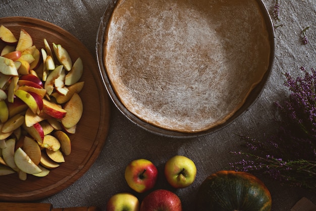 Vue de dessus d'une casserole avec de la pâte à tarte, une planche avec une lame de pommes et de citrouilles