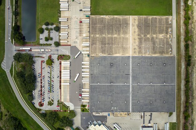 Vue de dessus d'un centre logistique géant avec de nombreux camions-remorques commerciaux déchargeant et téléchargeant des produits de détail pour une expédition ultérieure Concept d'économie mondiale