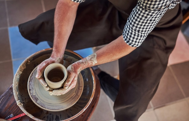 Photo vue de dessus. le céramiste utilise un tour de potier et crée un produit en argile fait à la main.