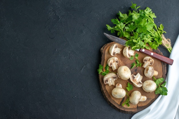 Vue de dessus des champignons crus et couteaux verts sur une serviette blanche en bois sur fond noir avec espace libre