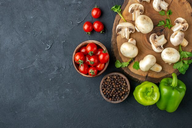 Vue de dessus des champignons crus et du couteau vert sur une serviette blanche en bois et des légumes frais sur le côté gauche sur fond noir