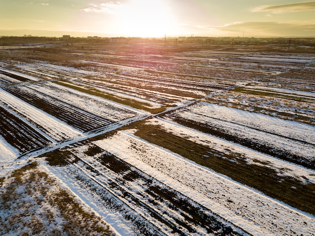 Vue de dessus des champs enneigés vides paysage rapiécé, horizon sombre et ciel lumineux le jour d'hiver ensoleillé. Concept de photographie de drone aérien.