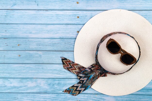 Vue de dessus d'un chapeau blanc de paille avec des lunettes allongé sur un fond en bois bleu. Concept de vacances d'été