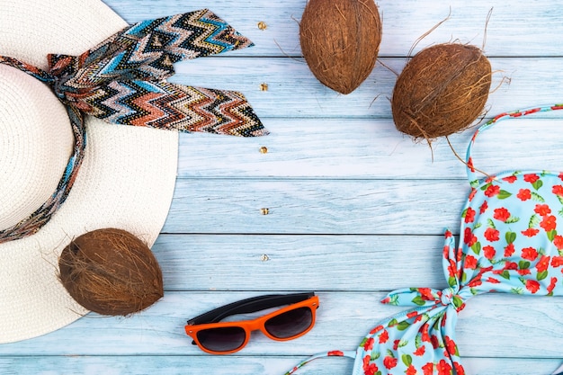 Vue de dessus d'un chapeau blanc de paille avec des lunettes, un maillot de bain et une noix de coco allongée sur un fond en bois bleu. Concept de vacances d'été.