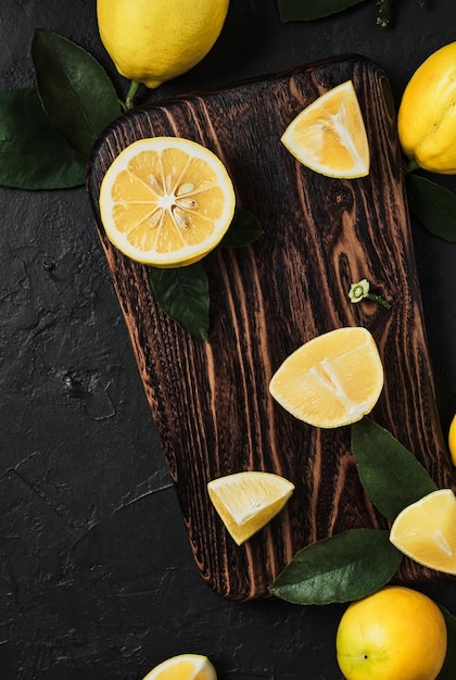 Vue de dessus des citrons frais et mûrs et des tranches d'agrumes sur une planche à découper en bois. Arrangement d'agrumes juteux sur une table en ciment ou en pierre sombre.