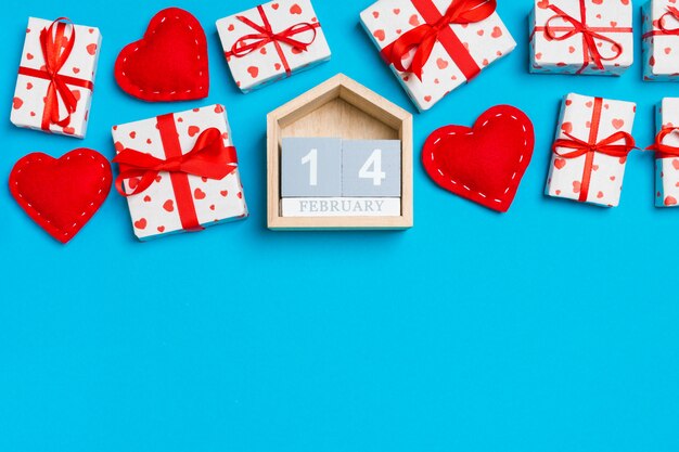 Vue de dessus des coffrets cadeaux, calendrier en bois et coeurs en textile rouge sur table. Le 14 février.