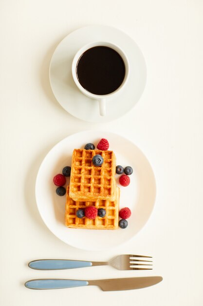 Vue de dessus à composition minimale de gaufres dessert sucré avec garniture de baies à côté d'une seule tasse de café noir