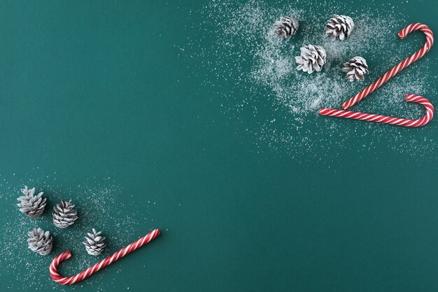 Vue de dessus de la composition de Noël de cônes de sapin enneigé, décorations de bonbons rouges sur bleu vert