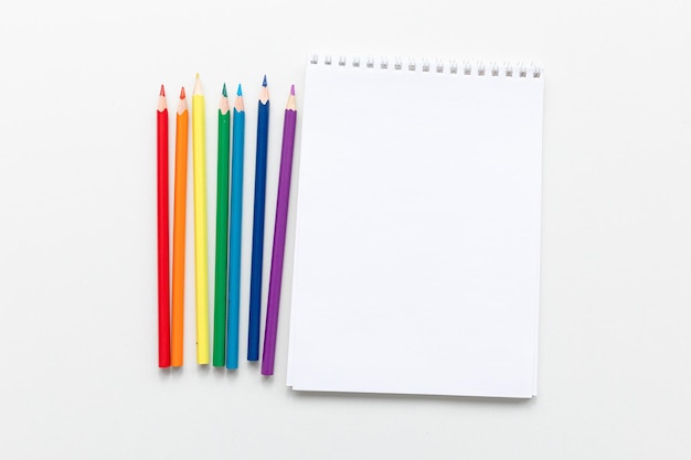 Vue de dessus Conception minimale d'un ordinateur portable ouvert avec des crayons de couleur de couleurs arc-en-ciel sur fond blanc avec un espace vide Mise à plat