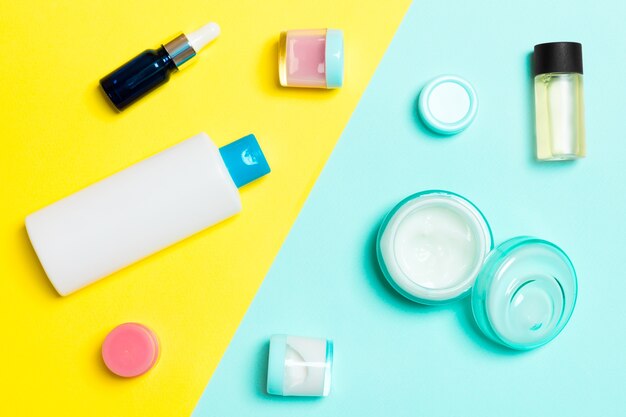 Photo vue de dessus des contenants cosmétiques, des sprays, des pots et des bouteilles sur fond jaune et bleu. vue rapprochée avec un espace vide pour votre conception.