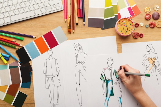 Vue de dessus sur le créateur de mode au travail. Mains féminines dessinant un croquis de vêtements dans son espace de travail créatif, vue de dessus