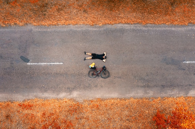 Vue de dessus d'un cycliste avec un vélo de route allongé sur l'asphalte.