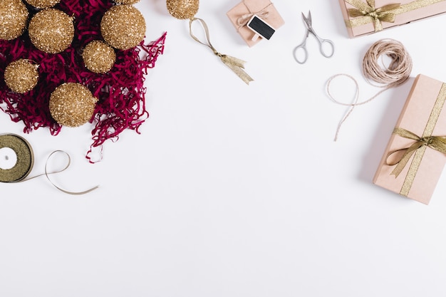 Vue de dessus des décorations de Noël, des boîtes avec des cadeaux, des ciseaux et des rubans sur un tableau blanc