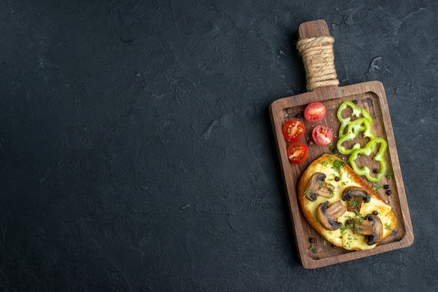 Vue de dessus d'une délicieuse collation faite maison avec des champignons et des légumes hachés sur le côté gauche sur une planche de bois sur fond noir