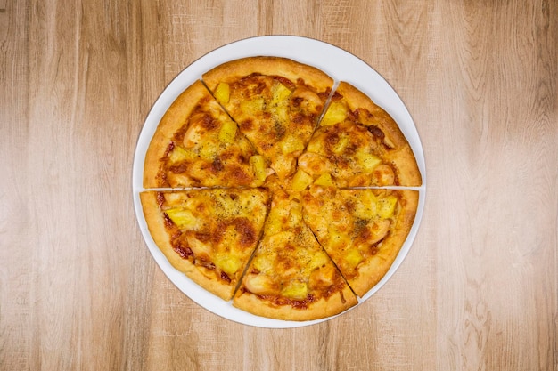 Vue de dessus d'une délicieuse et croustillante garniture de pizza hawaïenne avec du fromage mozzarella, de l'ananas et de la tomate sur fond de table de texture en bois.