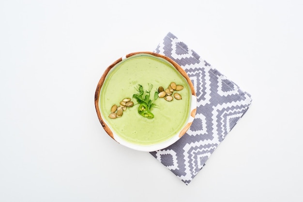 Vue de dessus d'une délicieuse soupe de légumes verts crémeux avec des germes et des graines de citrouille sur une serviette isolée