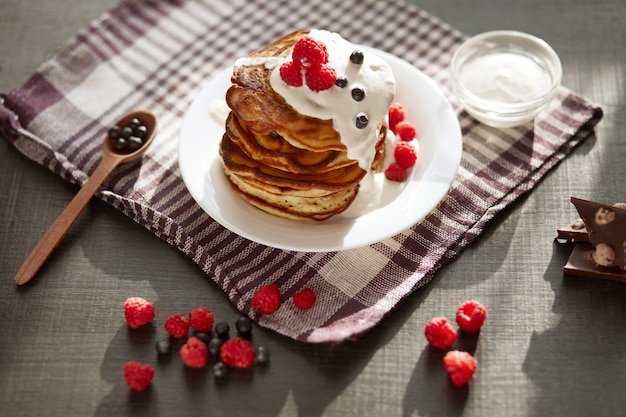 Vue de dessus de délicieuses crêpes aux bleuets et framboises sur une table brun foncé, tasse de thé ou de café, cuillère en bois avec des baies fraîches