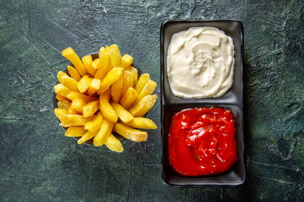 Vue de dessus de délicieuses frites avec des assaisonnements sur une surface sombre