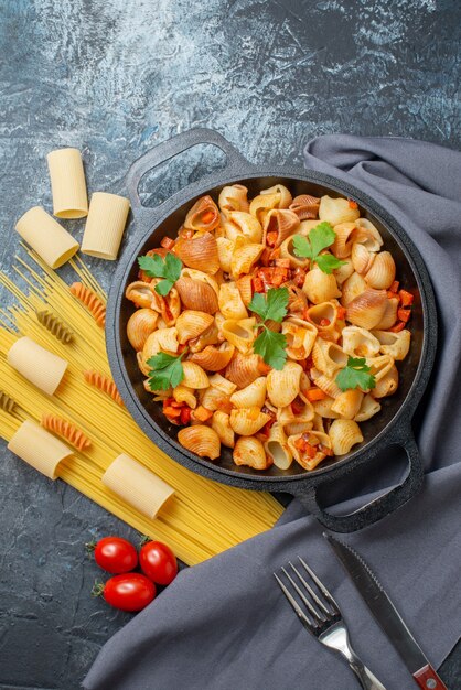 vue de dessus de délicieuses pâtes dans une poêle à frire spaghetti rigatoni spirales tomates cerises couteau et fourchette sur fond gris